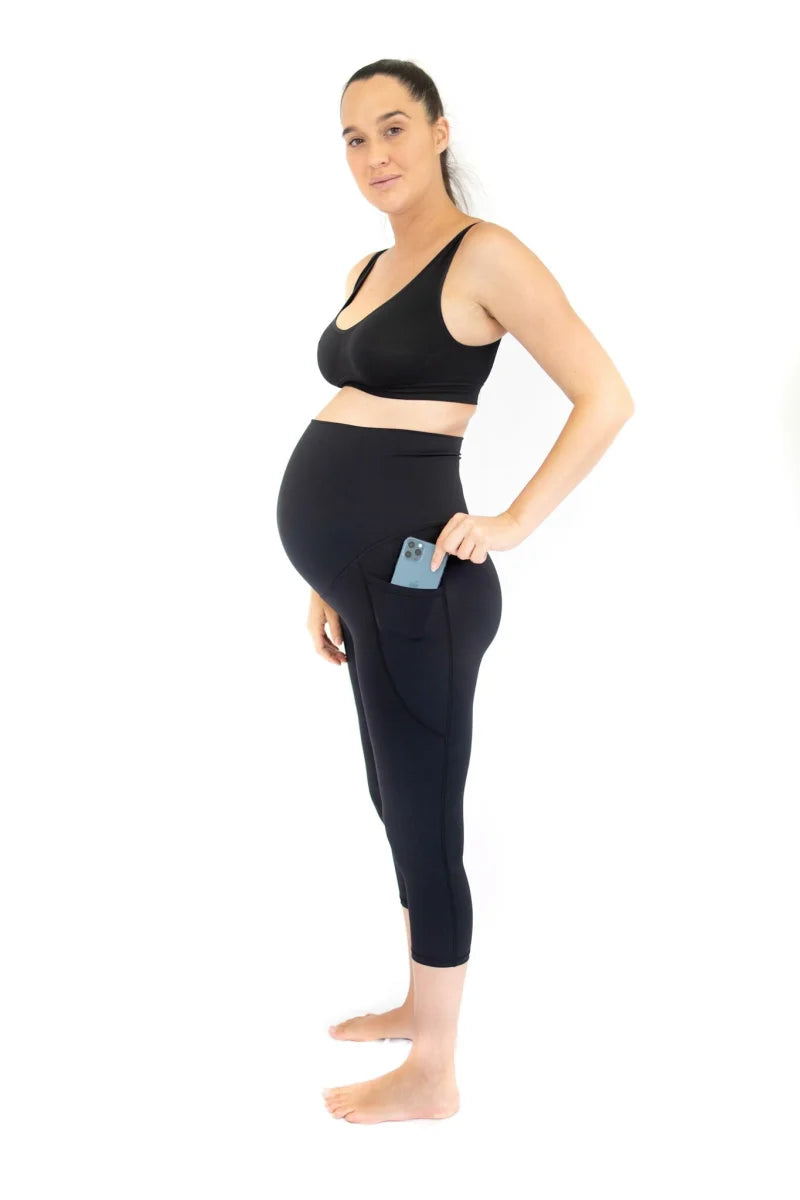 Pregnant woman in black maternity leggings, holding smartphone, for active mothers