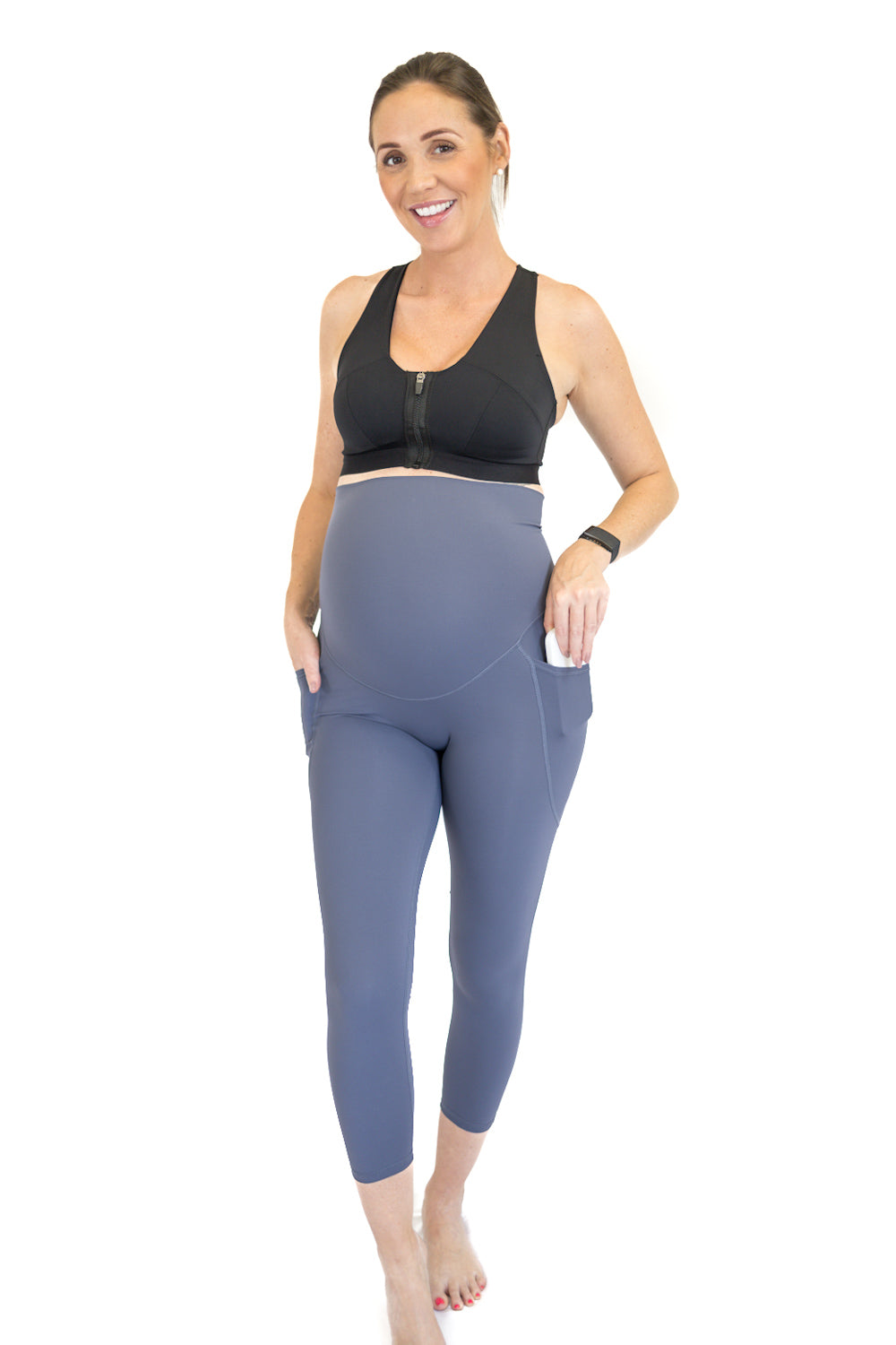 Smiling woman in black sports bra and blue 7/8 Pocket Emamaco maternity leggings