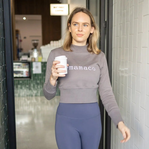 Person in crisp charcoal grey Mamaco sweatshirt and navy leggings holding coffee cup.