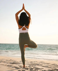 Silhouetted figure in activewear performing prenatal yoga tree pose on the beach.