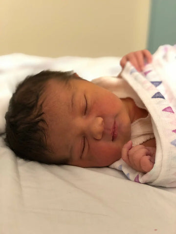 Sleeping newborn baby in a white onesie, reflecting on infant feeding choices for exclusively breastfed kids.