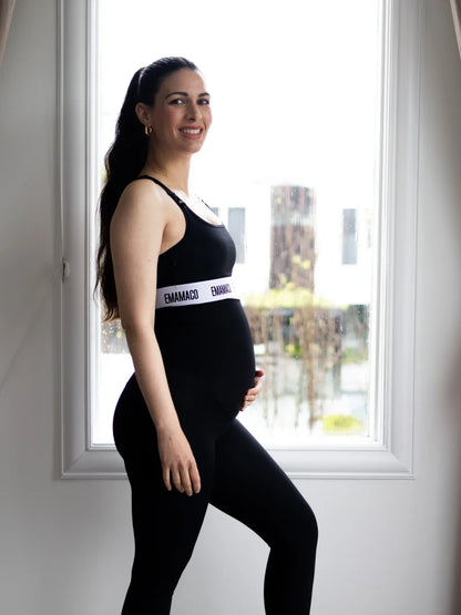 Pregnant woman in black athletic wear with Aware Nursing Sports Bra by window