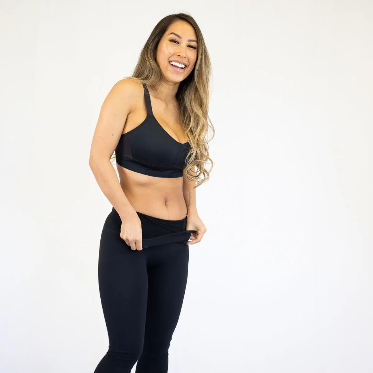 Woman in black shapewear leggings with pockets, smiling while showcasing body shapewear