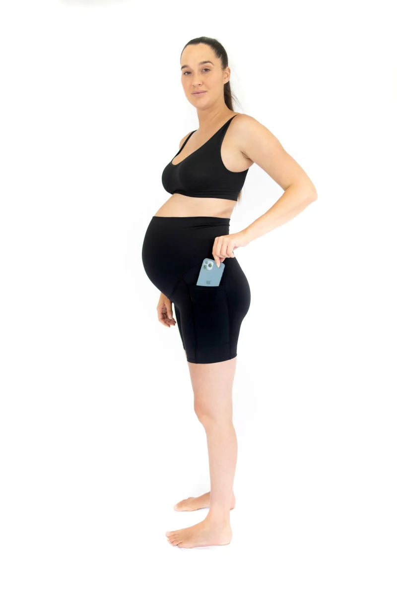 Pregnant woman in black Emama Maternity Bike Shorts with pockets holding a blue object