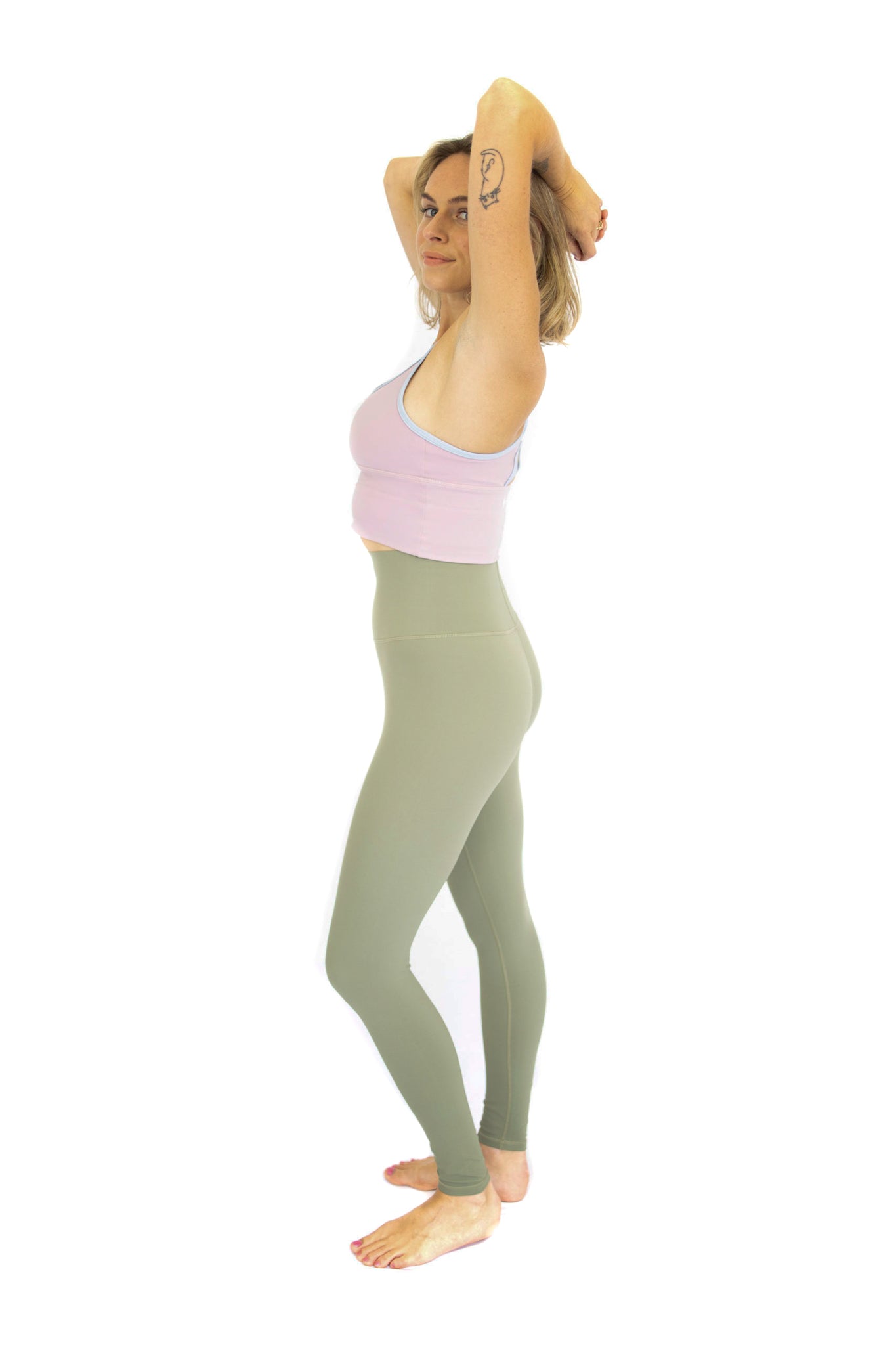 Woman in activewear stretching with arms raised, showcasing Shaper Move Leggings in Olive