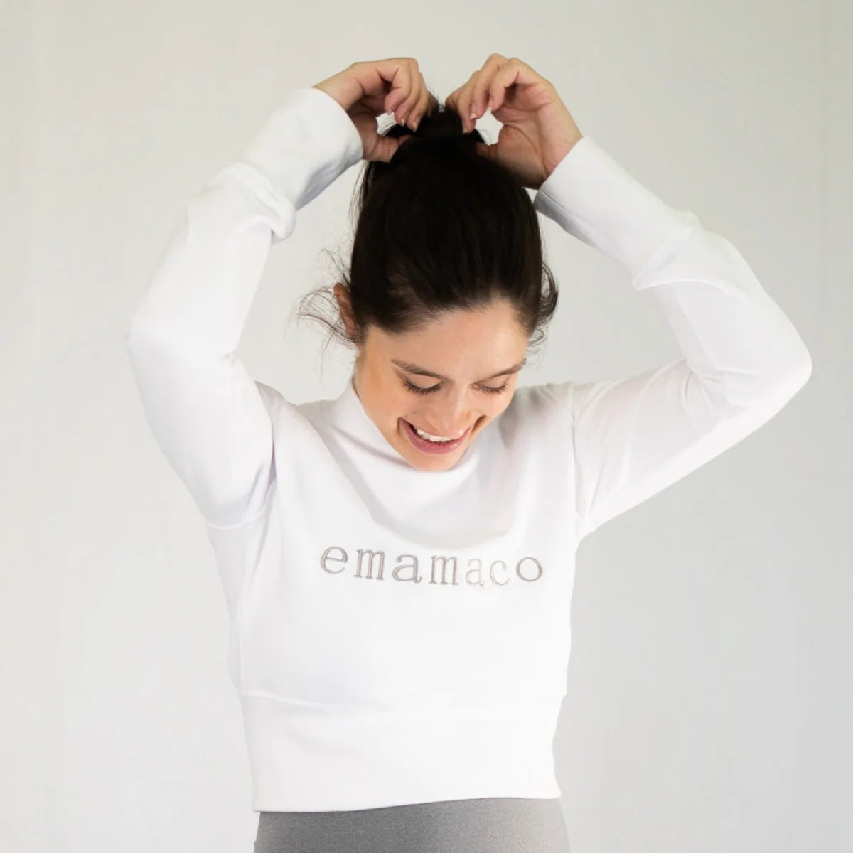 Woman wearing Snow High Neck Jumper with delicately stitched emamaco logo, tying hair up