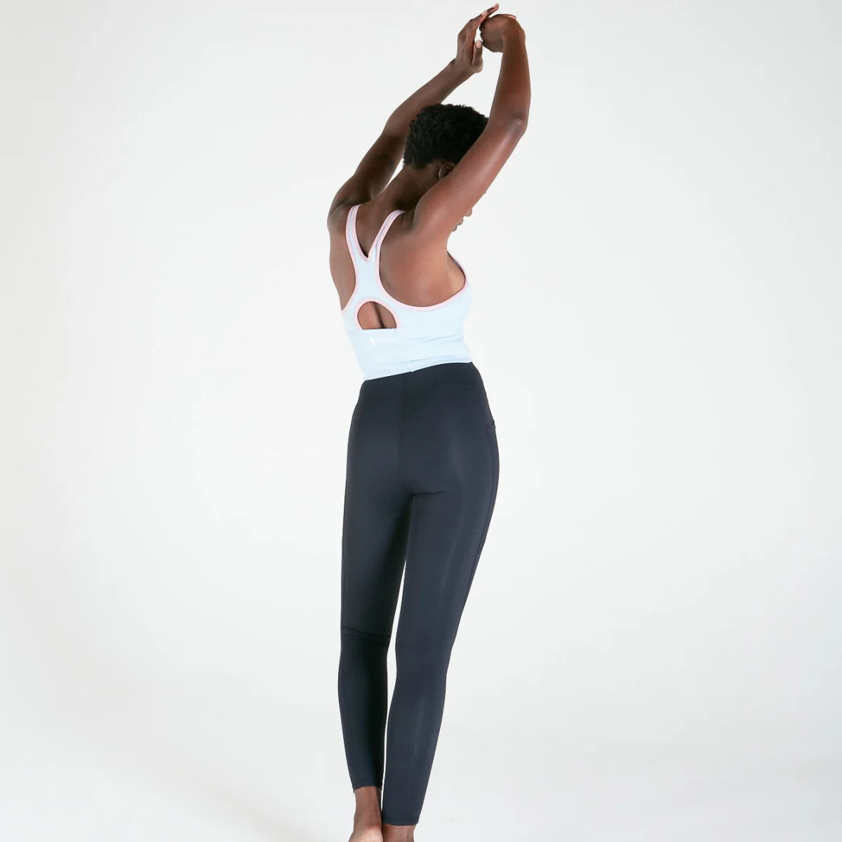 Woman in athletic wear stretching arms, showcasing Vibe Leggings with regular fit waistband